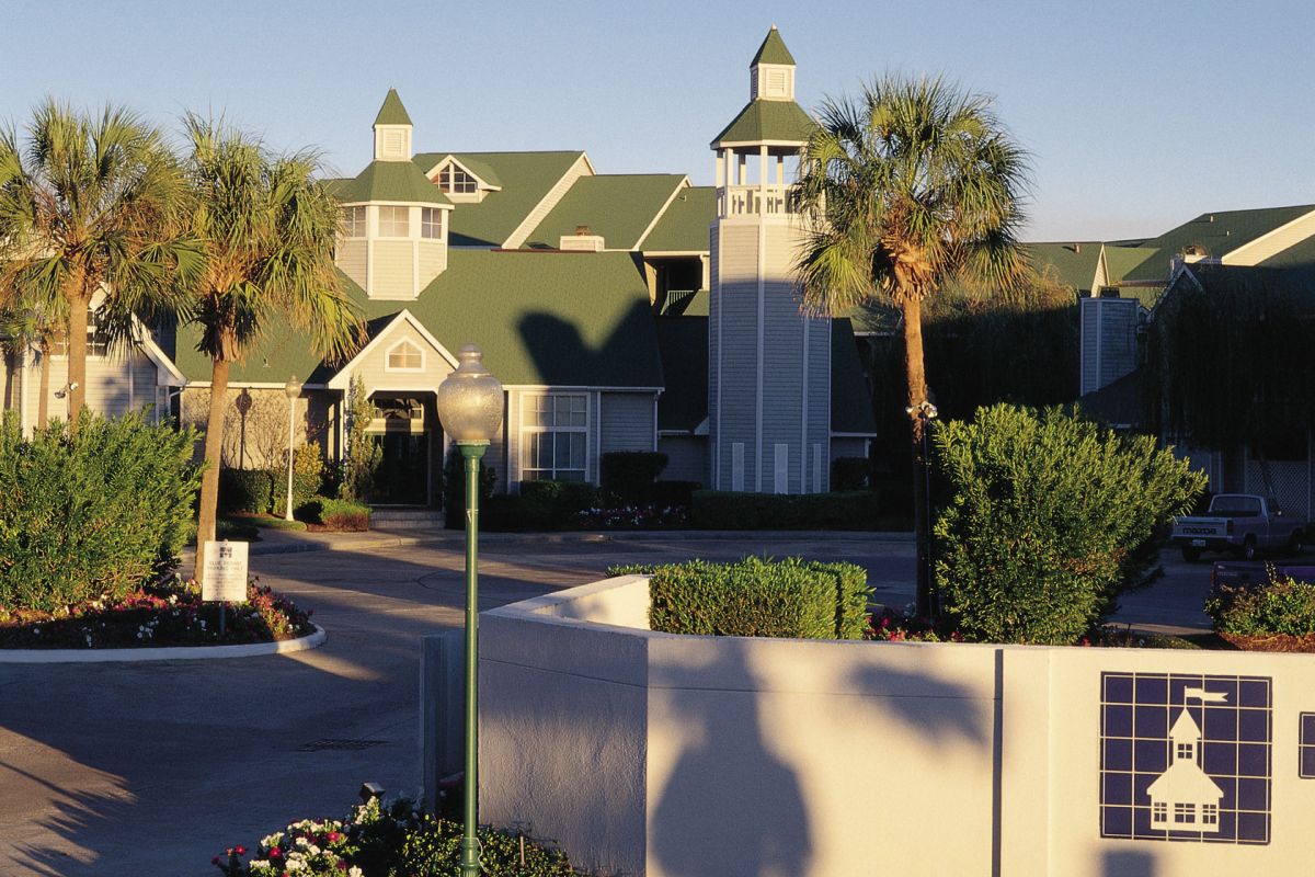 A hotel with green roofs, palm trees, and a white fence displaying the Hampton Inn logo near Broadwater resort.