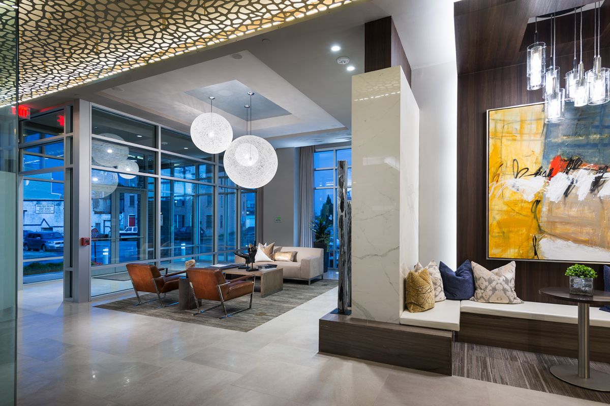 Modern lobby with leather chairs, abstract art, globe lights, and large windows showing city outside.