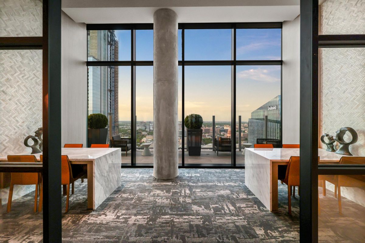 Modern office space with two desks, orange chairs, large windows, and cityscape view at sunset.