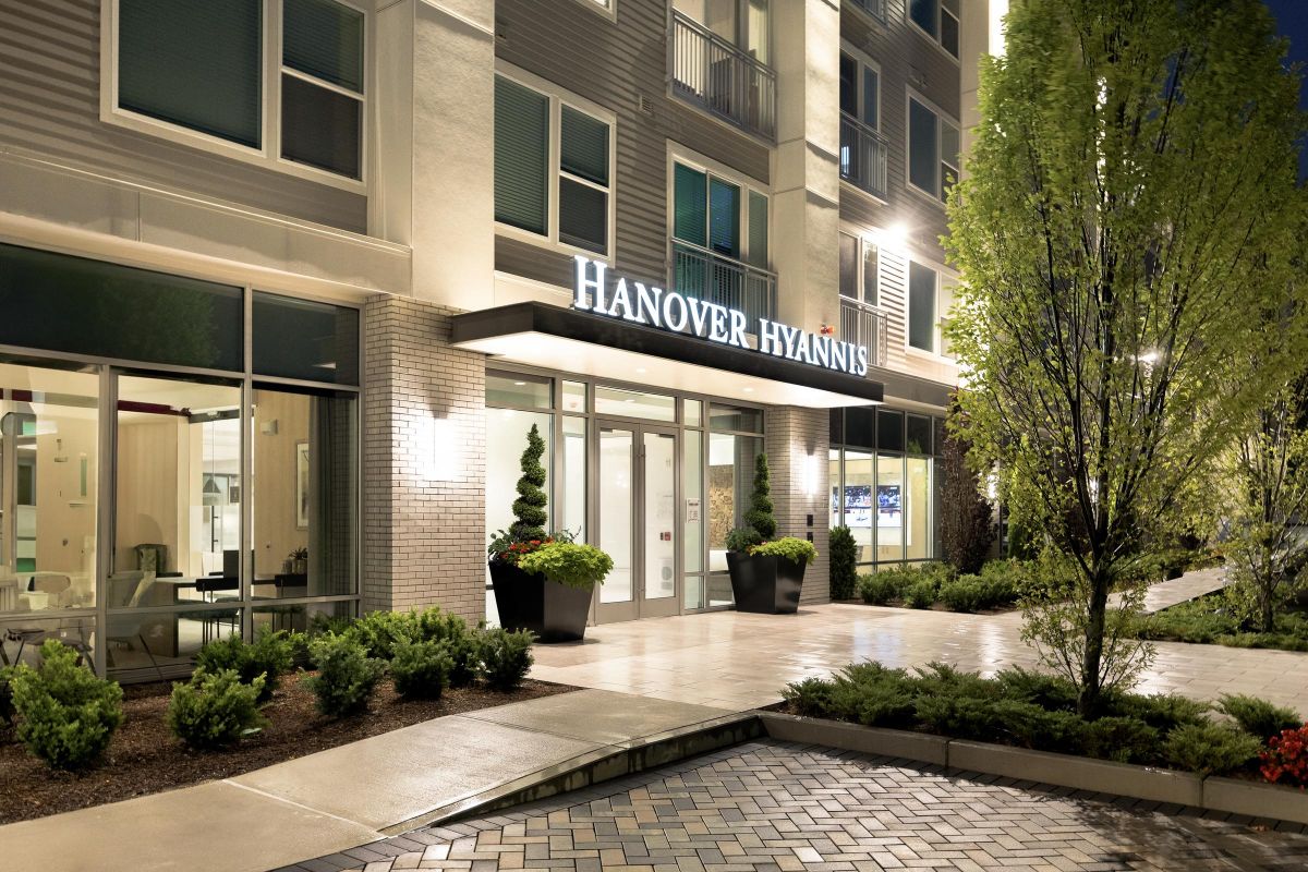 Night view of modern building entrance with "Hanover Hyannis" sign, greenery, and potted plants.