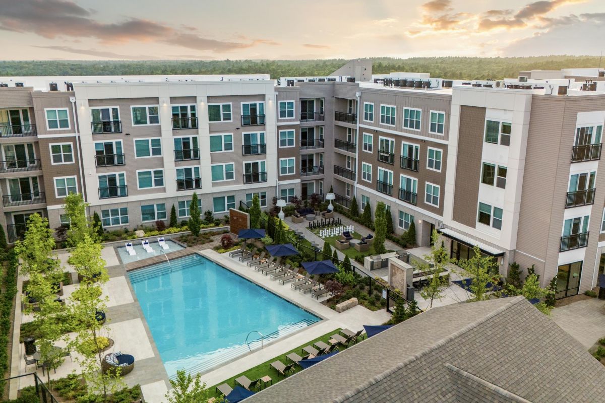 Aerial view of an apartment complex with a central courtyard pool, surrounded by greenery and lounge chairs.