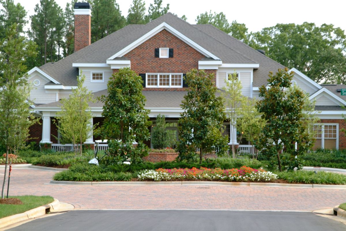 Large brick house with white trim, front porch, and landscaped garden with trees and flowers.
