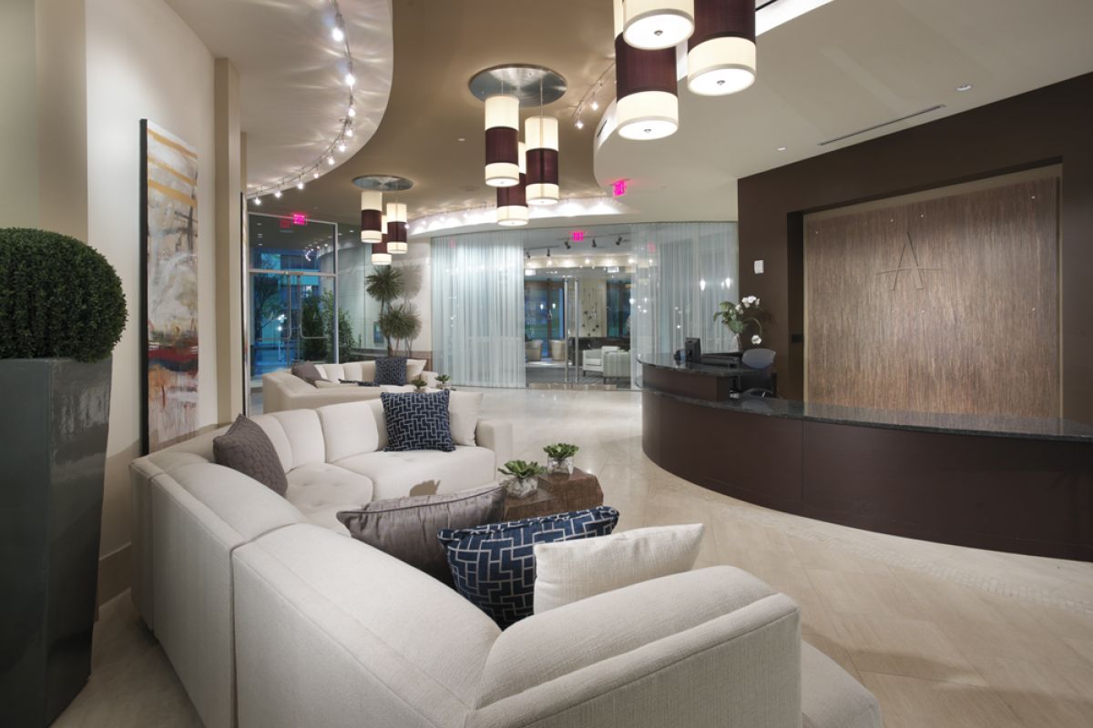 Modern, stylish Ashton Austin hotel lobby with curved sofas, decorative pillows, and a sleek reception desk under hanging lights.