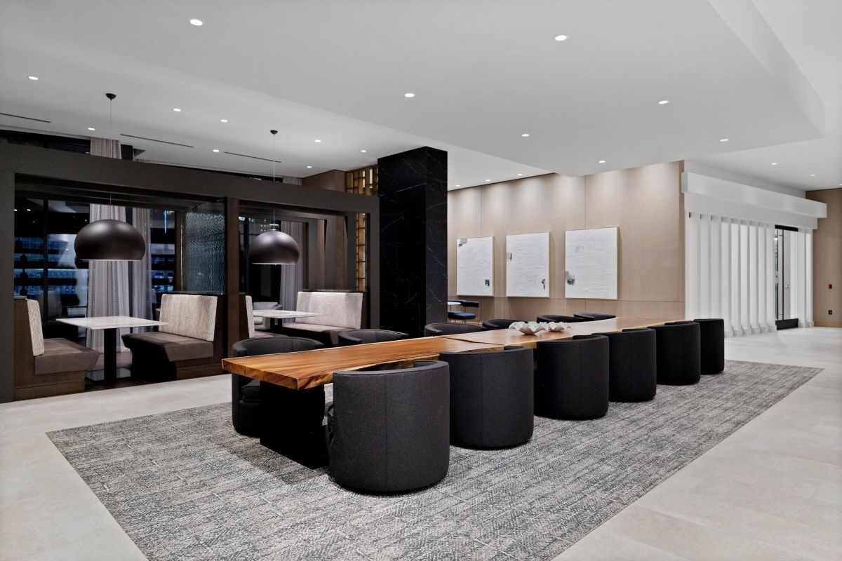 Modern meeting area with a long wooden table, black chairs, cozy booths, and pendant lights on a textured rug.