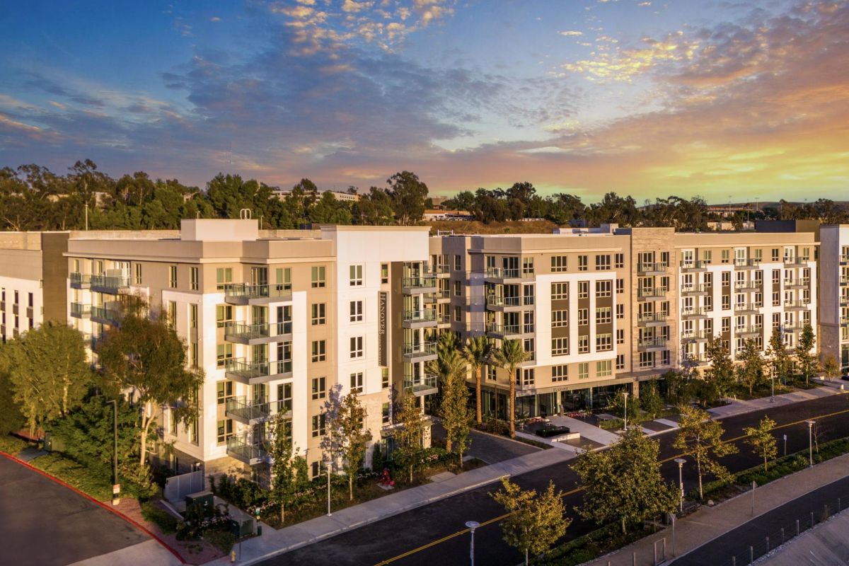 Hanover Company Modern apartment complex with greenery at sunset, featuring multiple floors and large windows.