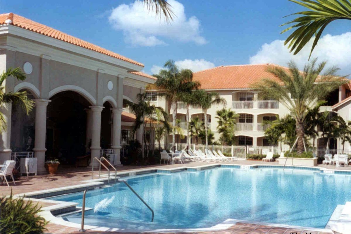 A resort-style pool with lounge chairs, palm trees, and a large Broadwater Galveston hotel under a blue sky.