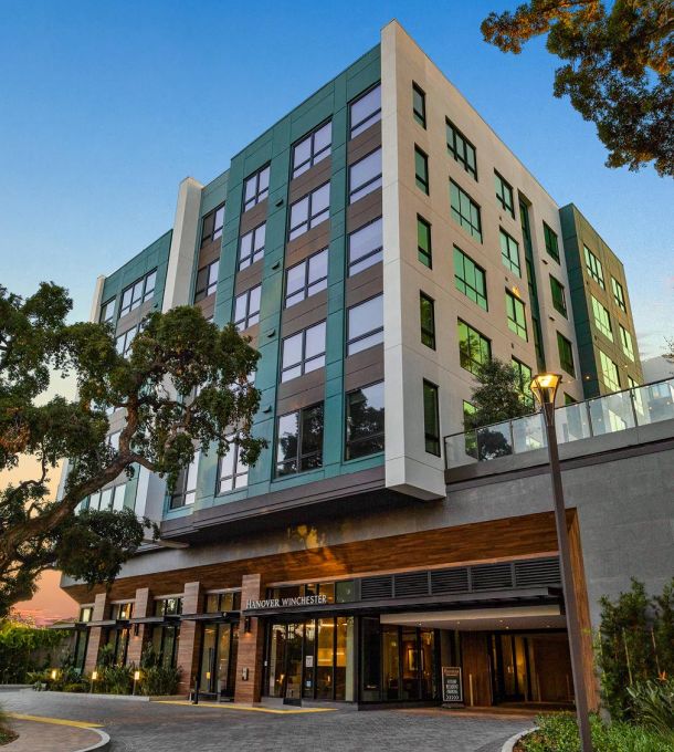 Modern mid-rise apartment building with large windows and trees in front, photographed at sunset.