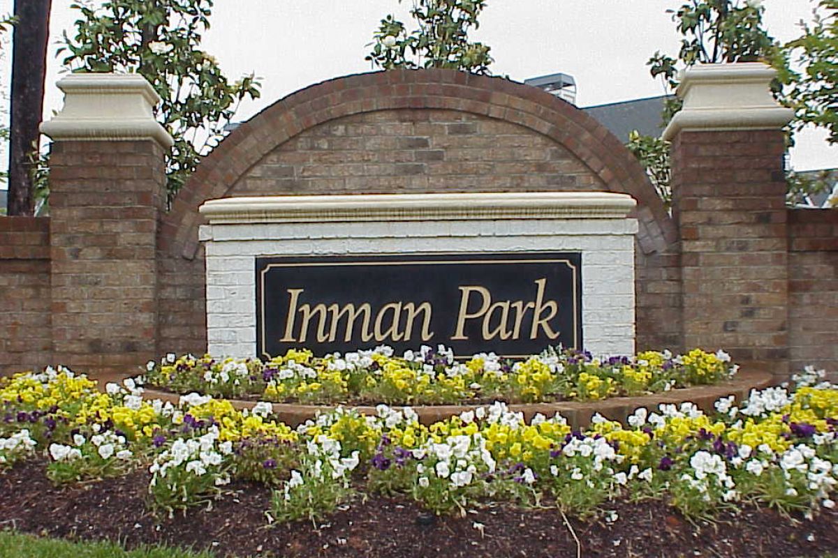 A brick sign reading "Inman Park" stands behind a bed of colorful flowers and greenery.