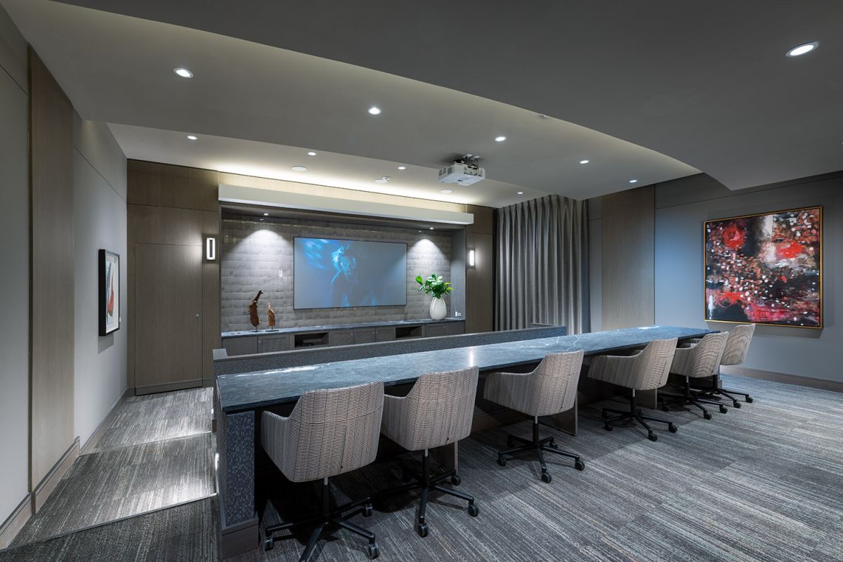 Modern conference room with long table, swivel chairs, projector screen, and contemporary artwork on walls.