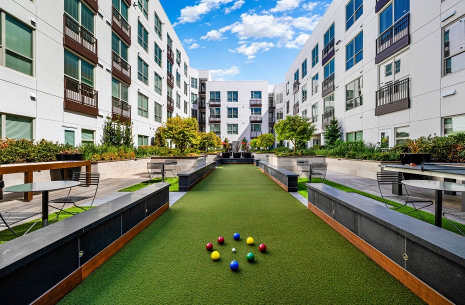 Hanover Company, Hanover Walnut Creek Courtyard with a bocce ball court, surrounded by modern apartment buildings and greenery under a blue sky.