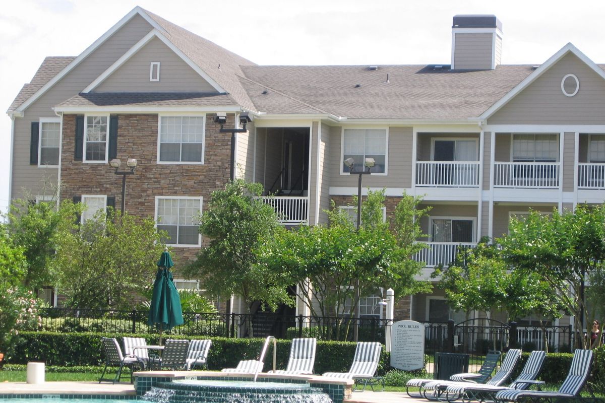 Lounge chairs by a pool at The Broadwater Galveston, set before a modern apartment building with balconies and trees.