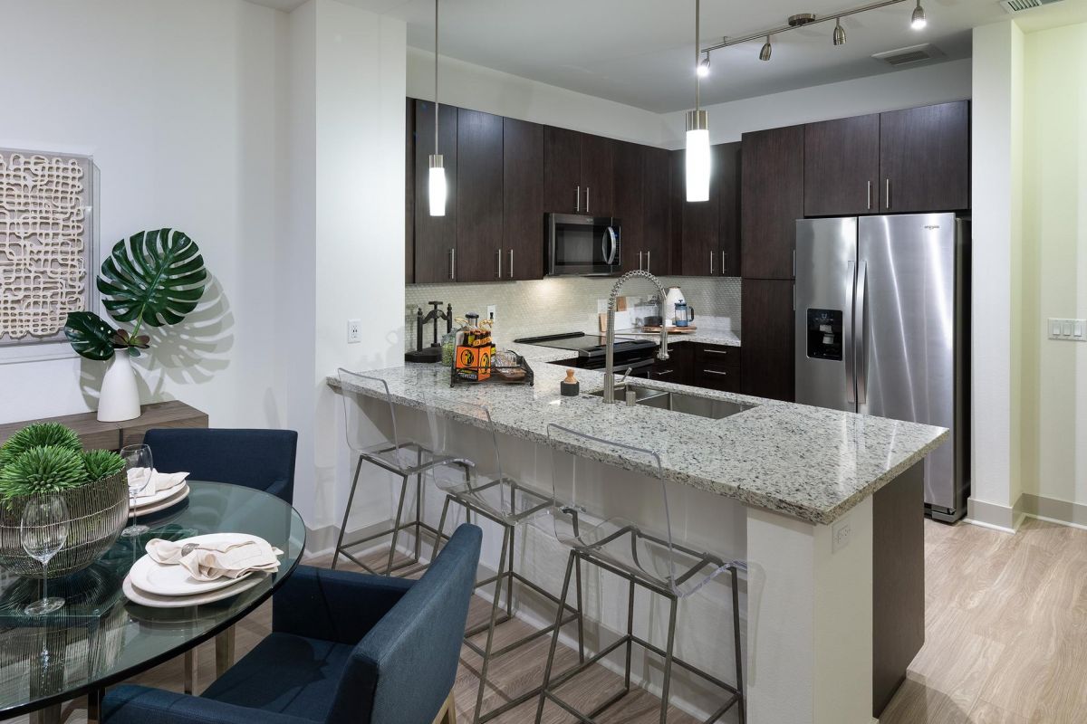 Modern kitchen with dark cabinets, stainless steel appliances, island seating, and dining area with blue chairs.