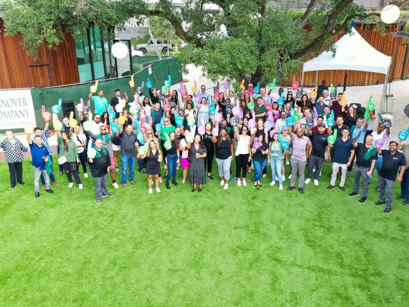 A large group of people smiling and posing together outside on a lawn, many holding foam fingers.