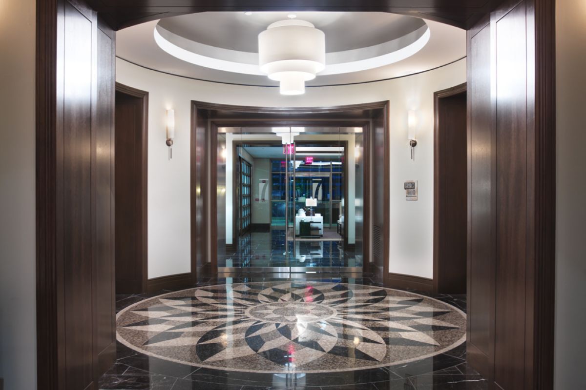 Elegant hallway with a marble floor medallion, wood accents, and modern circular ceiling lights.