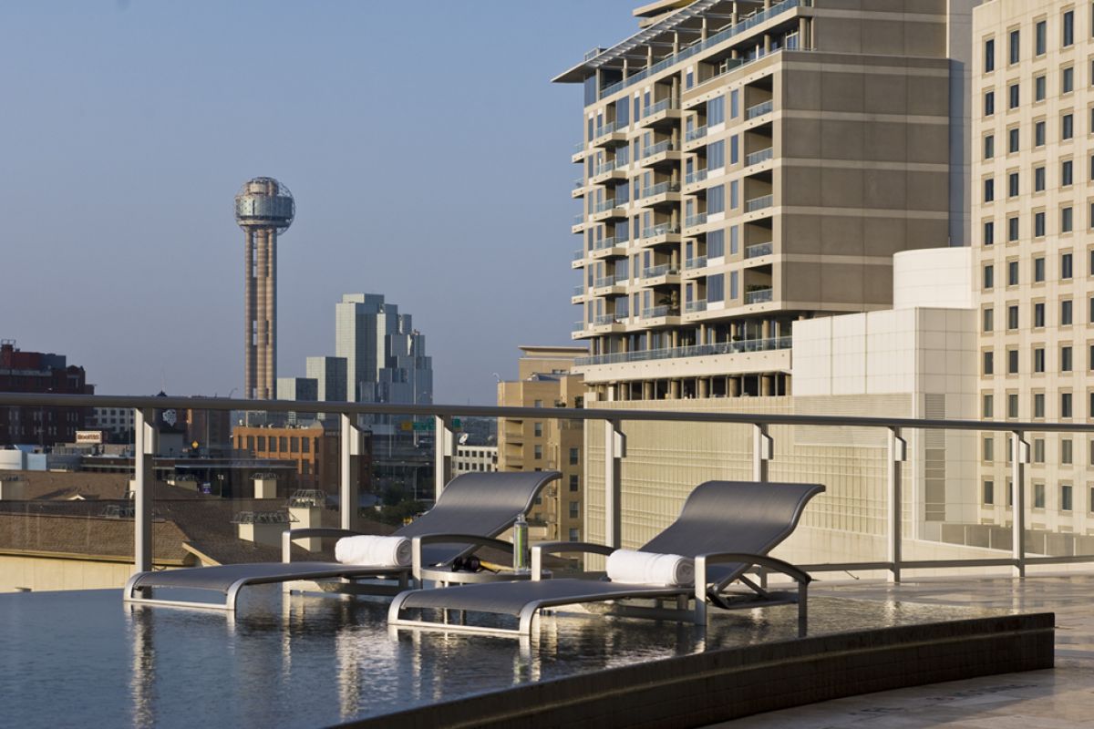 Two lounge chairs beside a rooftop pool with a city skyline and tower in the background.