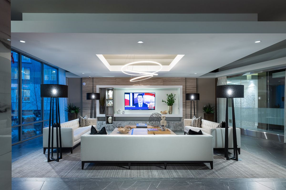 Modern lounge with white sofas, black floor lamps, a circular light fixture, and a TV on the wall.