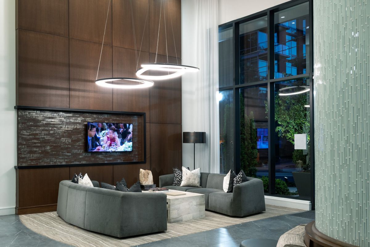 Modern lobby with gray sofas, a TV on a wood accent wall, large windows, and circular pendant lights.