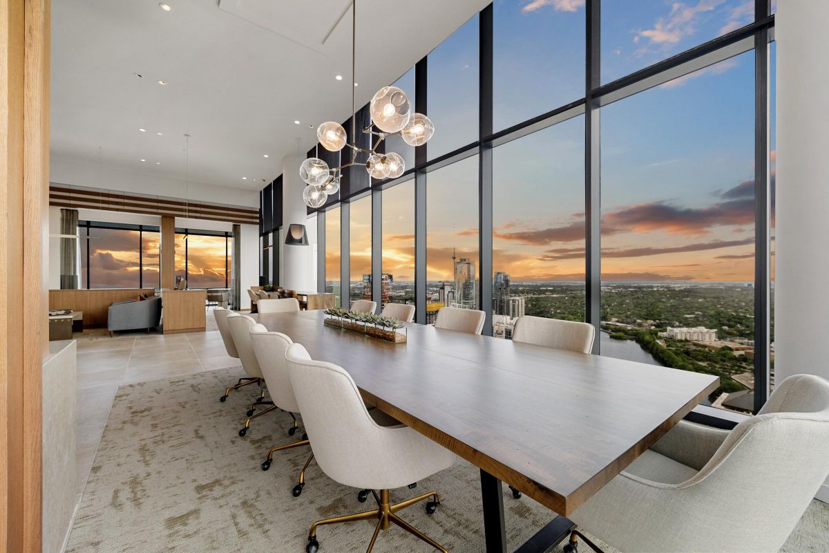 Modern dining room with floor-to-ceiling windows, sunset view, long table, and white chairs.