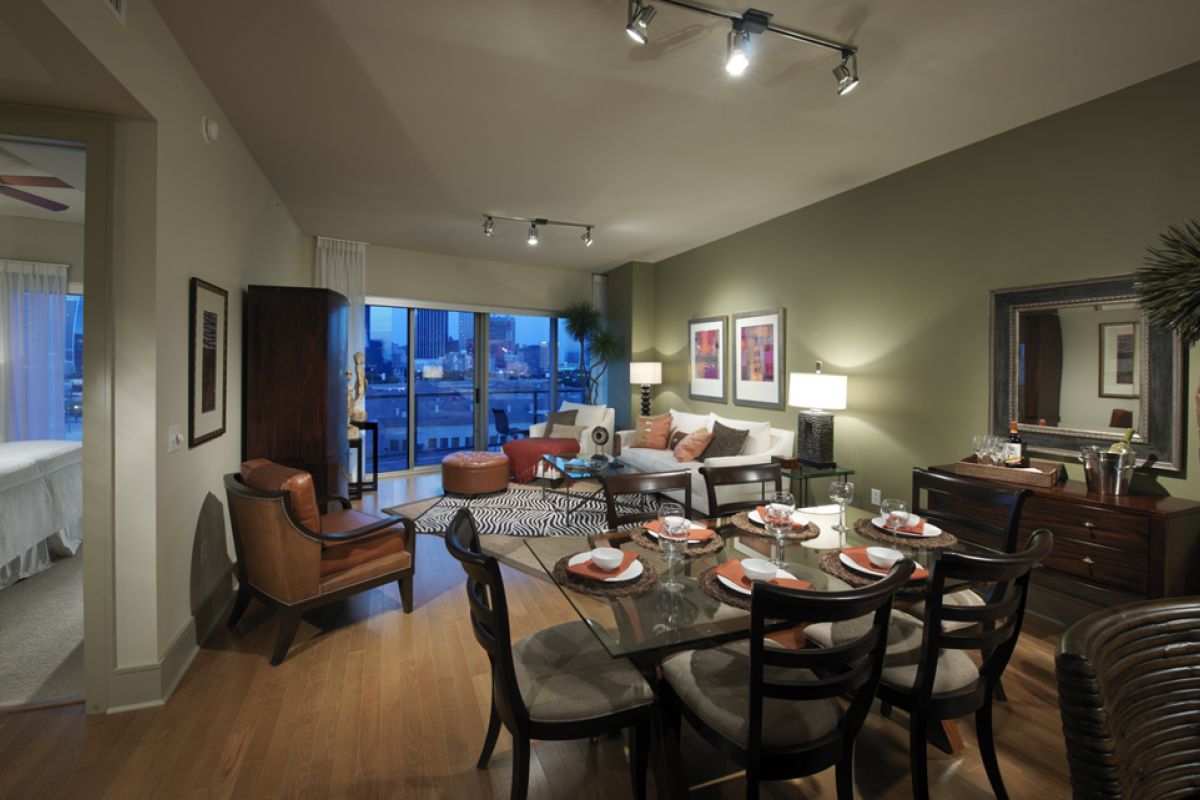 Modern apartment living and dining area with stylish decor, glass table, and large window showing city view.