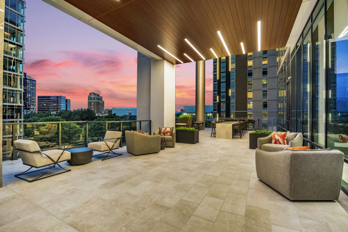 Rooftop terrace with modern seating and tables, cityscape view, and colorful sunset sky in the background.