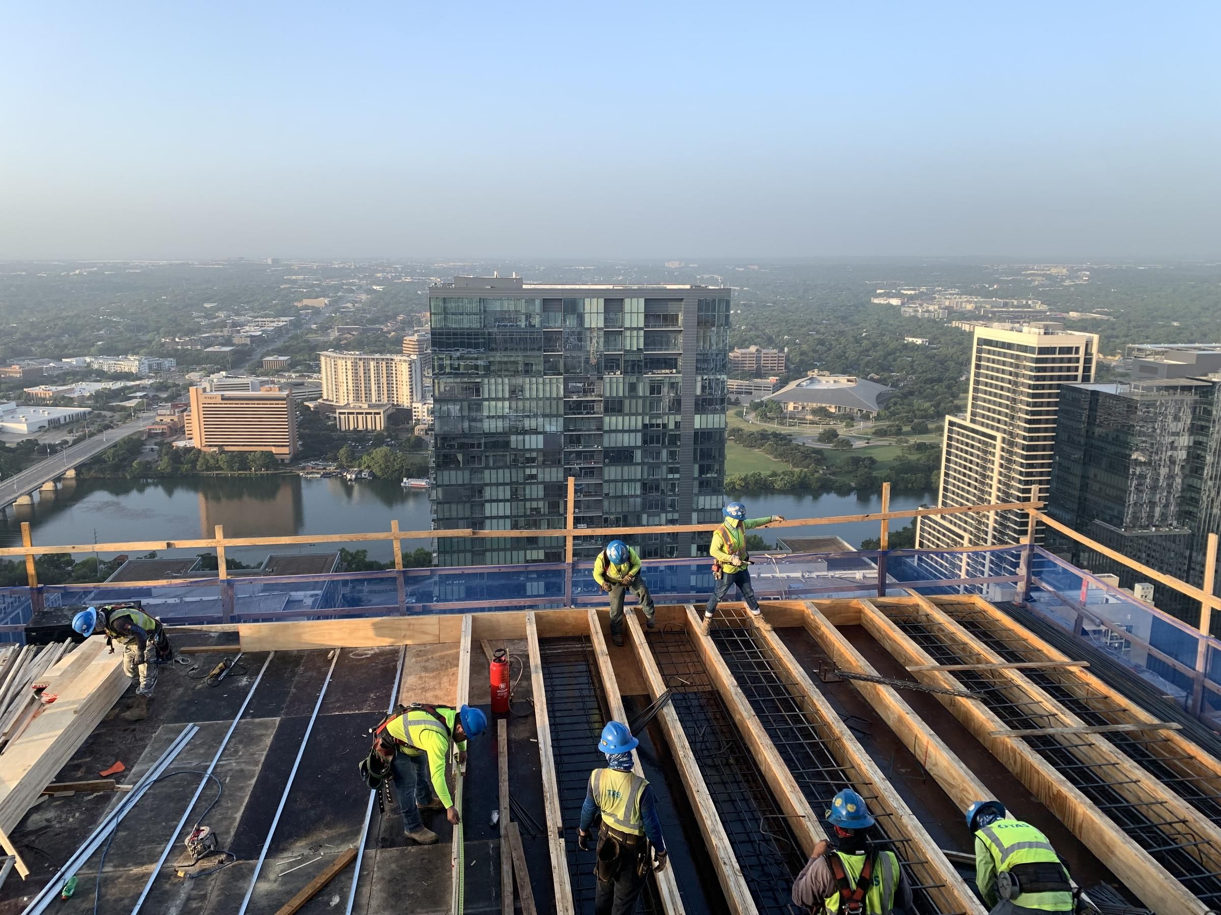 Workers in safety gear construct a building on a high-rise rooftop with a city skyline in the background a Hanover Corporate construction project.