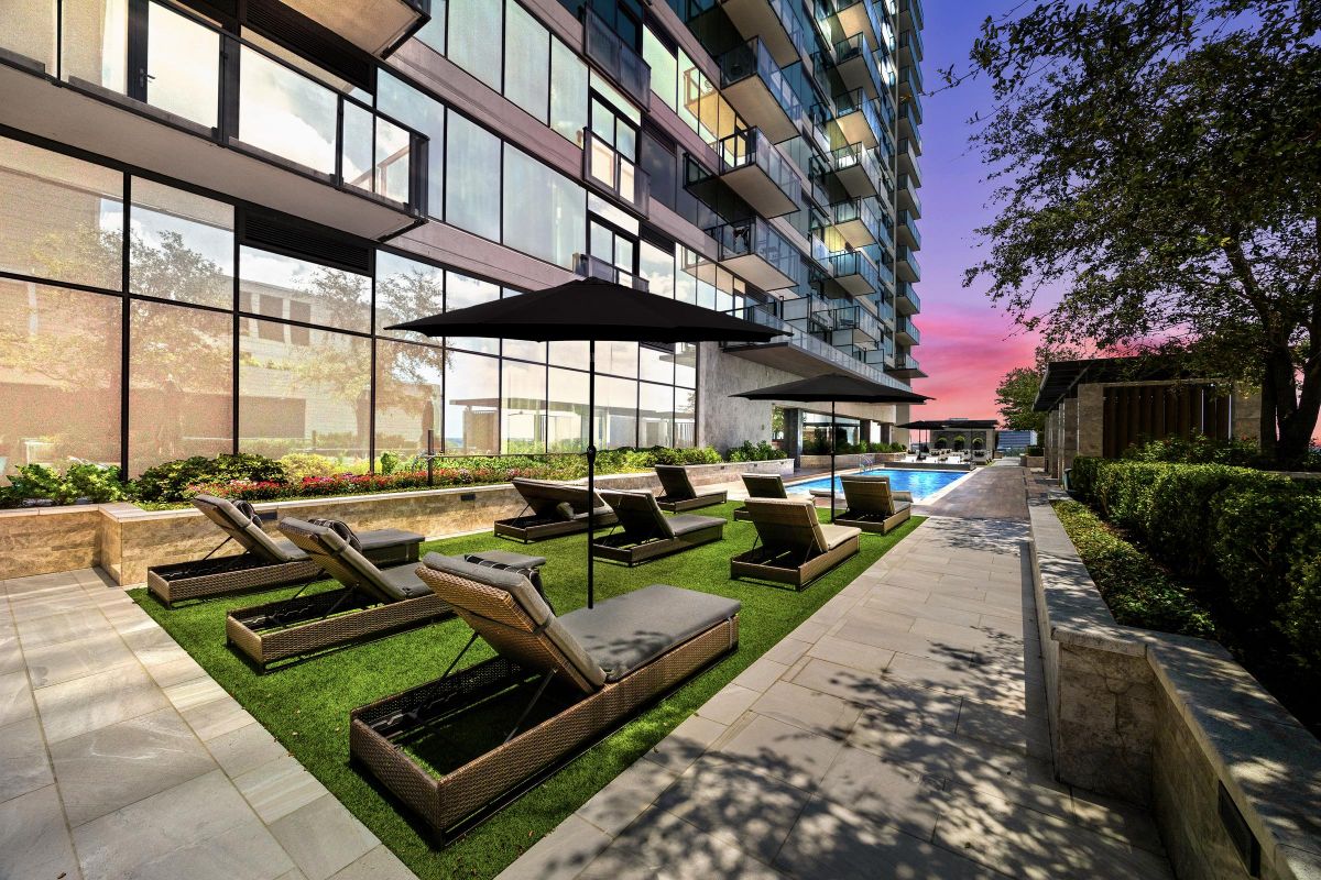 Outdoor lounge area with wicker chairs, umbrella, pool, and modern building at sunset.