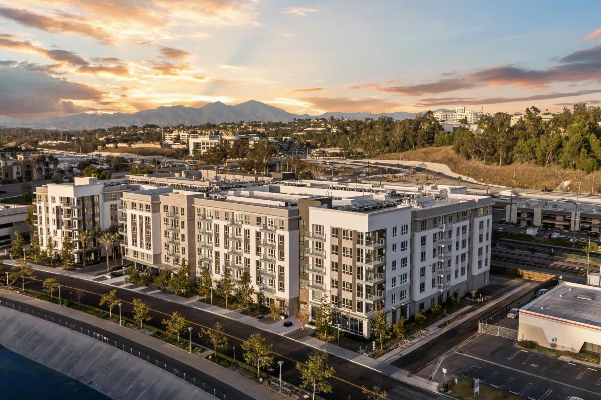 Hanover Laguna Niguel Aerial view of a modern apartment complex at sunset, with mountains and trees in the background.