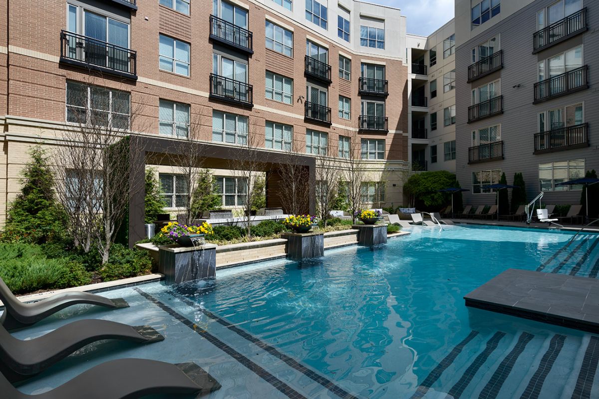 Modern courtyard at Hanover Exton Square with a pool, lounge chairs, and waterfall—experience true luxury apartment living.