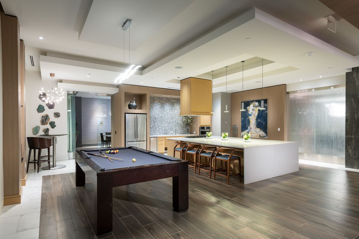 Modern open-concept kitchen and lounge with a pool table and bar seating, warmly lit at night.