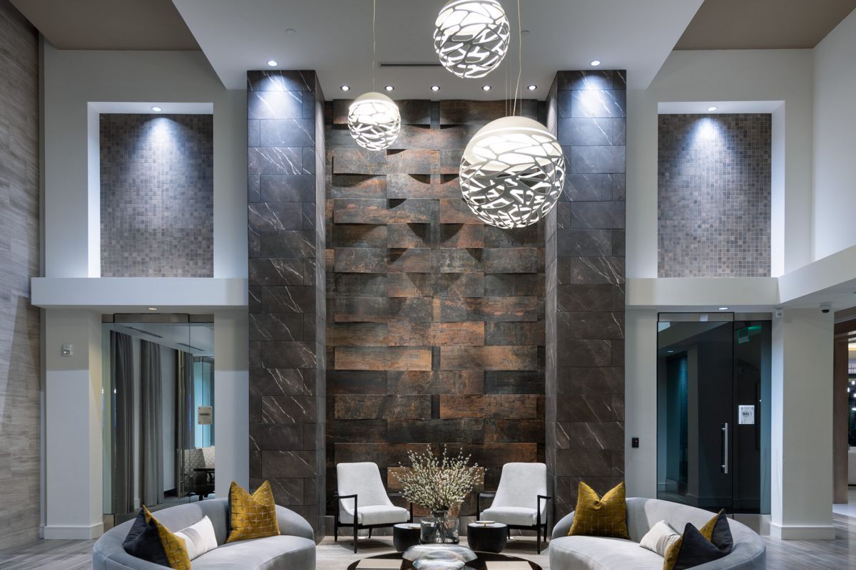 Modern lobby with curved sofas, round coffee table, and hanging pendant lights under a high ceiling.