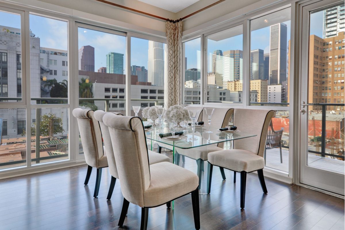 Modern dining room with glass table and beige chairs, large windows showing city skyline views.
