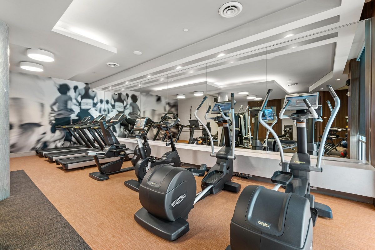 Modern gym interior with treadmills, elliptical machines, and a mirrored wall reflecting equipment.