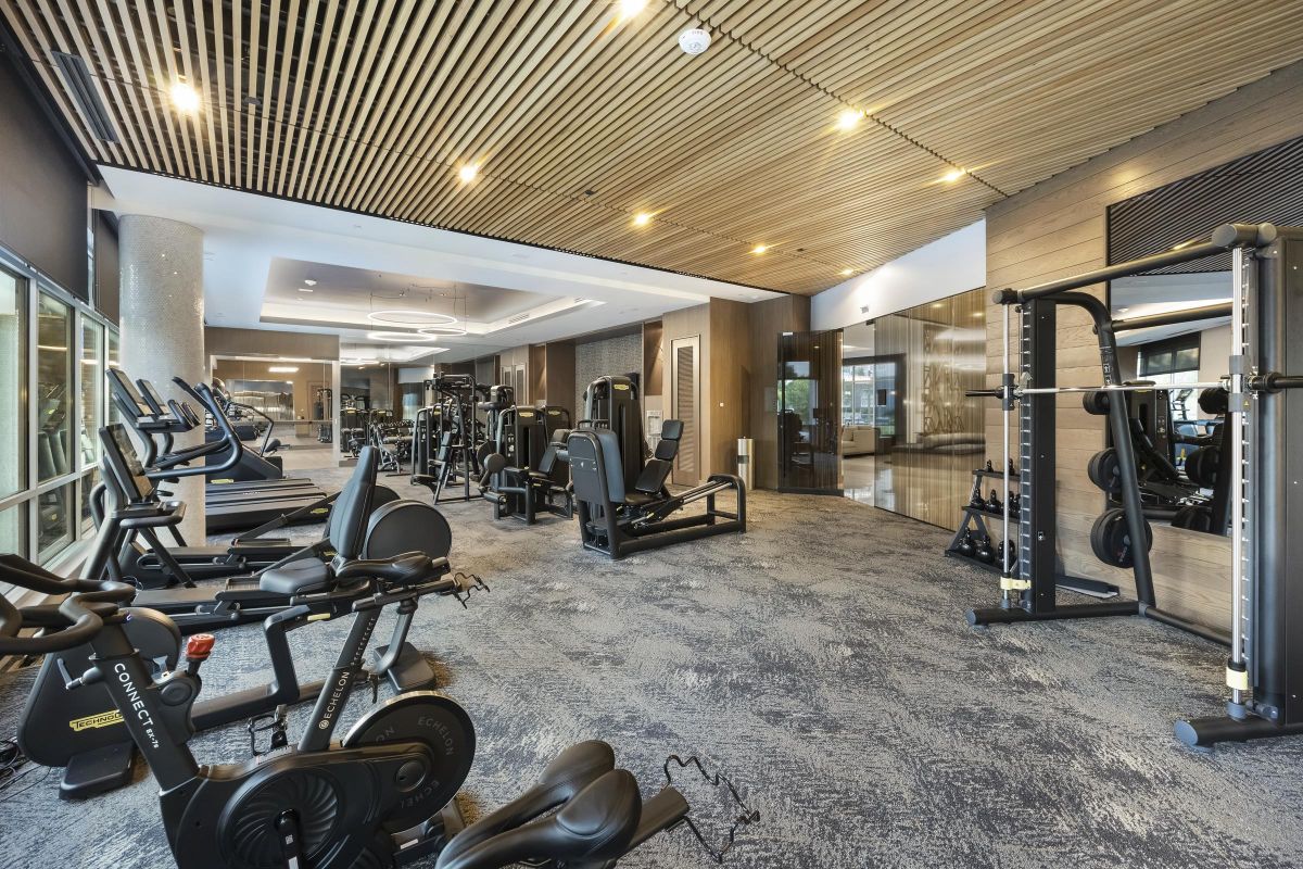 Modern gym with exercise equipment, including stationary bikes, treadmills, and weight machines, under wooden ceiling.