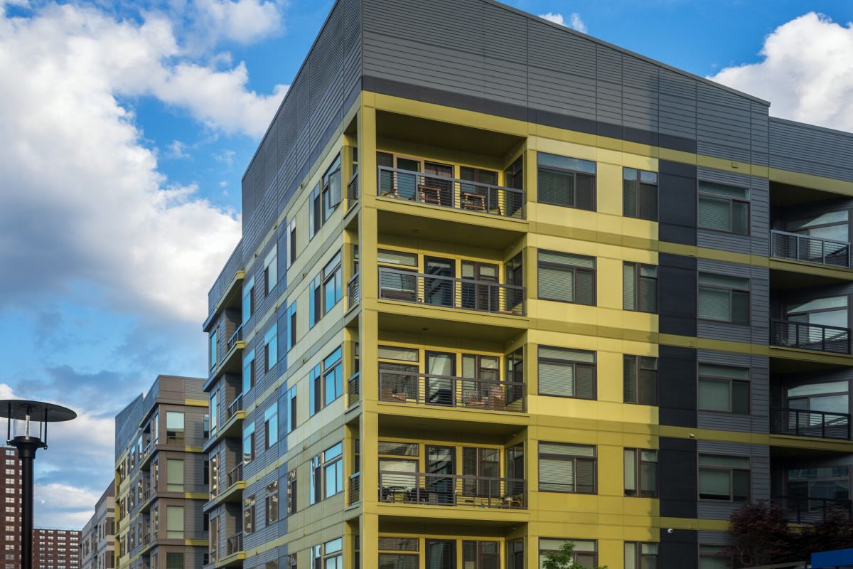 Modern yellow and gray apartment building under a bright blue sky with some clouds.