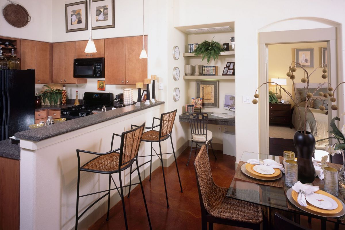 Modern apartment kitchen with bar stools, a dining table set for two, and a small built-in desk area.