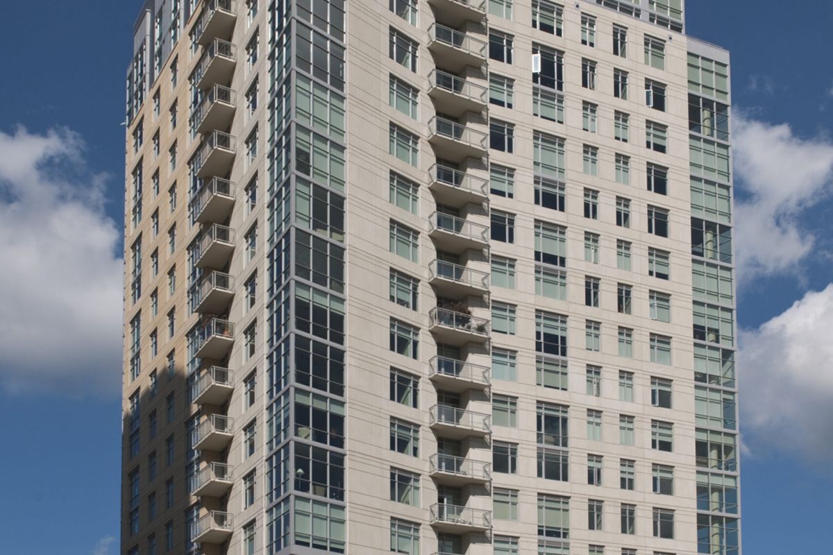 Tall modern apartment building with balconies on a sunny day, located at a city street intersection.