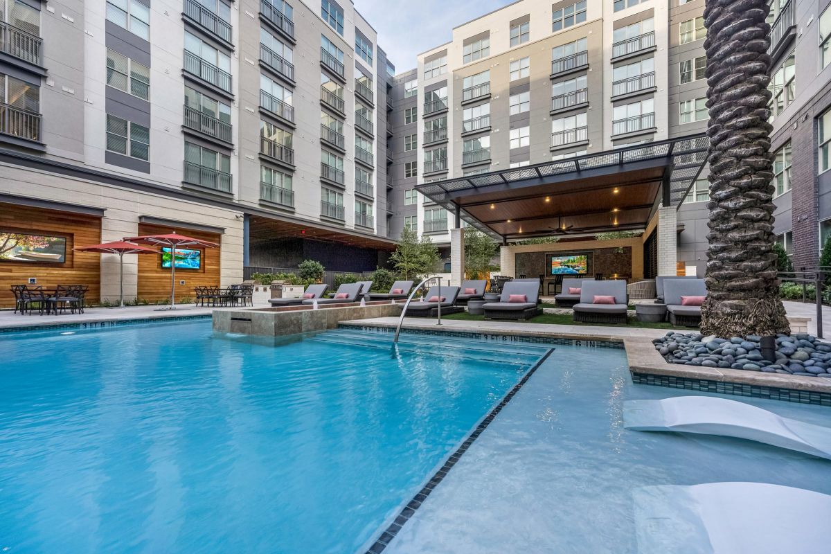 Modern apartment pool area with lounge chairs, umbrellas, and covered seating in a courtyard.
