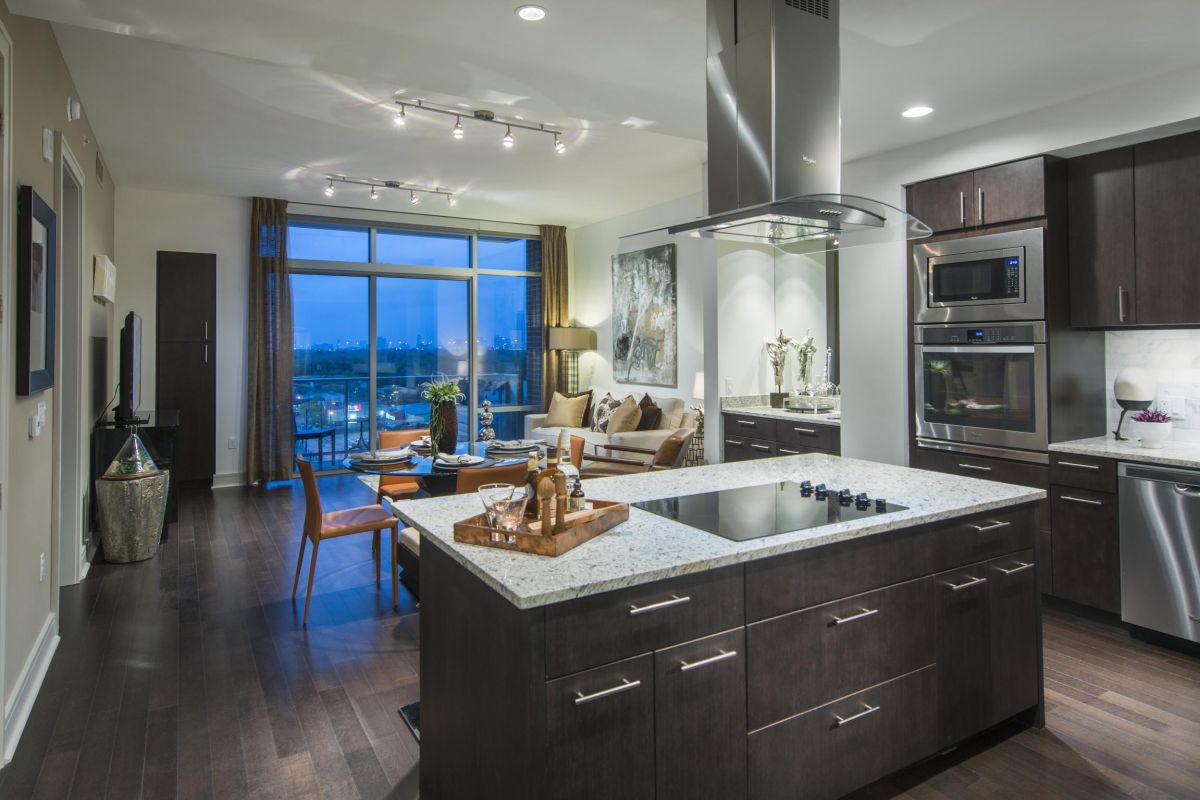 Modern kitchen with dark wood cabinets, marble island, and a city view through large windows.