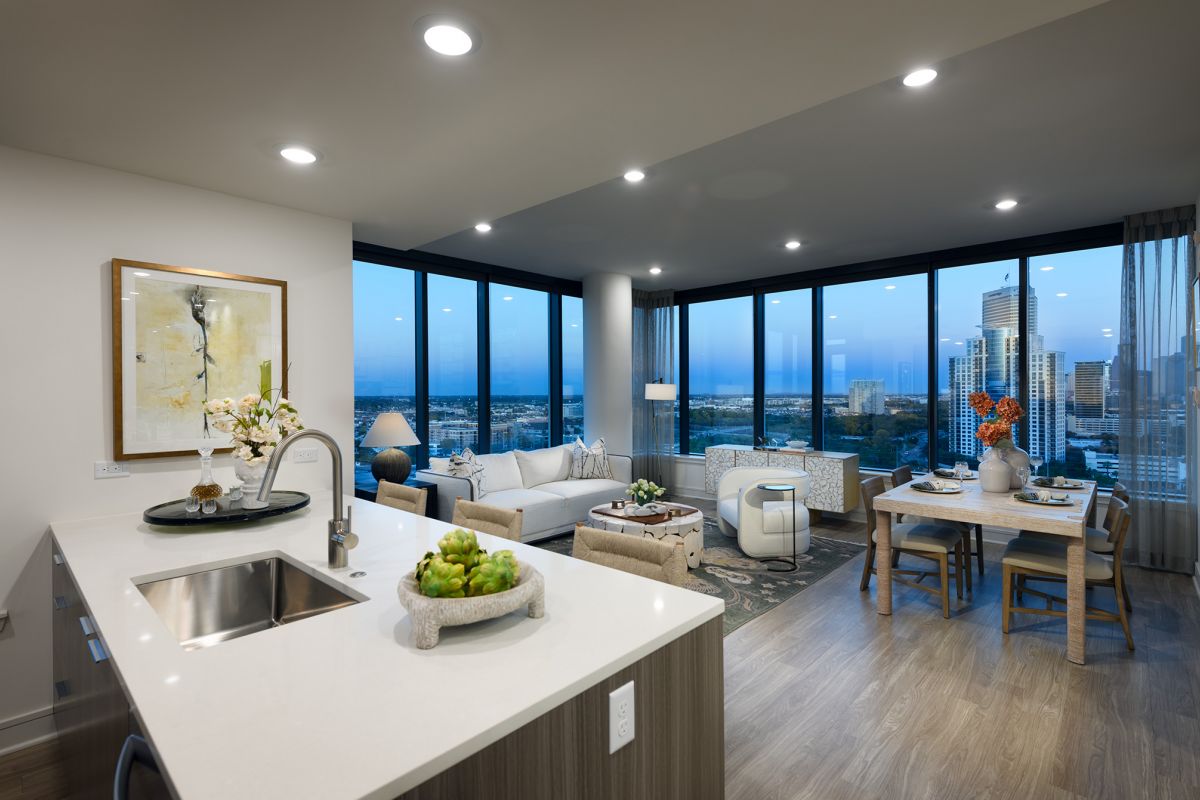 Modern Hanover high-rise apartment with open kitchen, spacious living area, and large windows overlooking Buffalo Bayou at dusk.