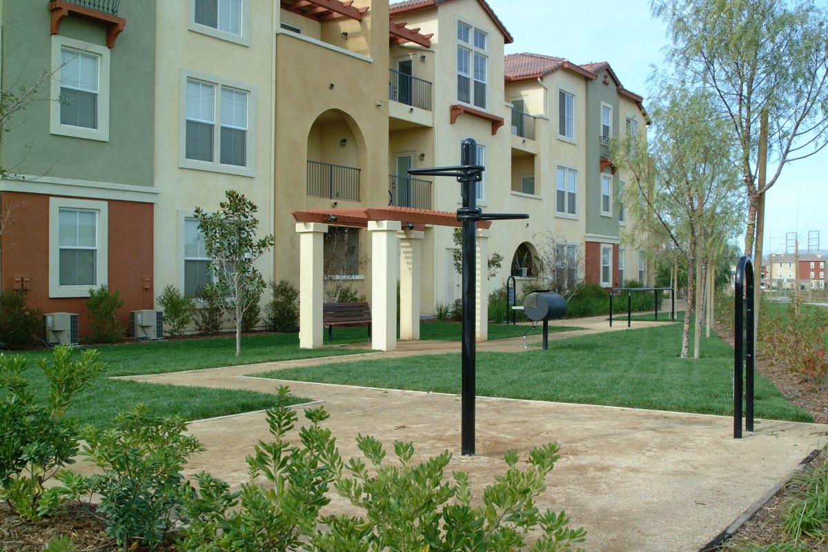 Outdoor fitness area with pull-up bars and a grill in front of a multi-story apartment building.