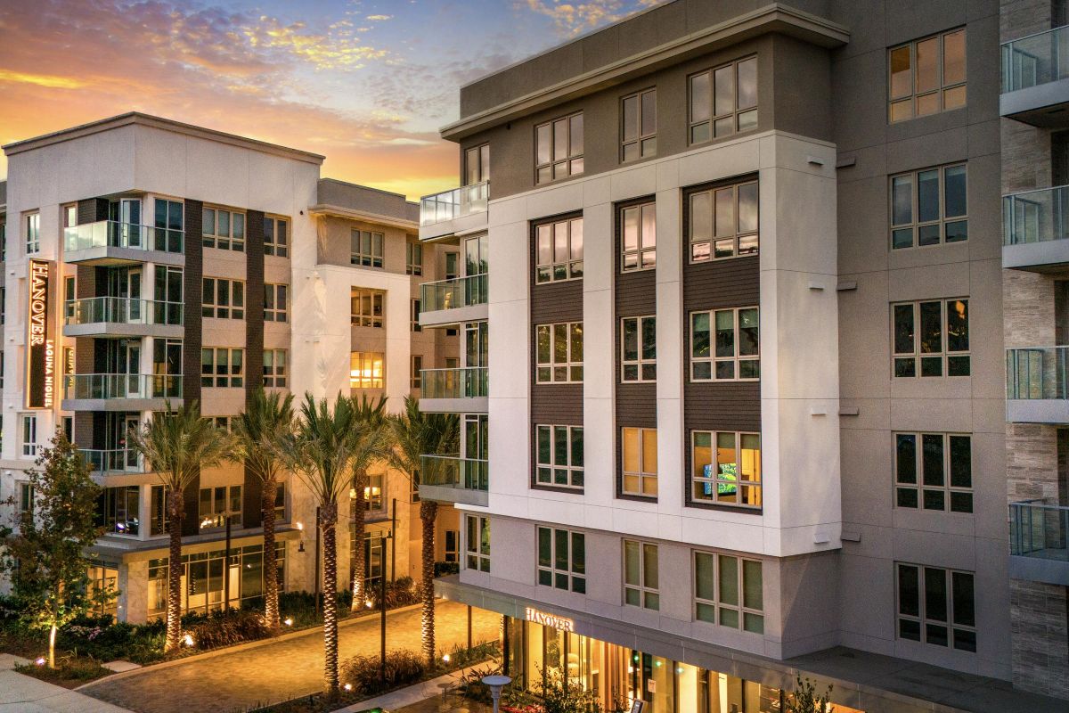 Hanover Laguna Niguel Modern apartment complex with palm trees at sunset, featuring balconies and large windows.