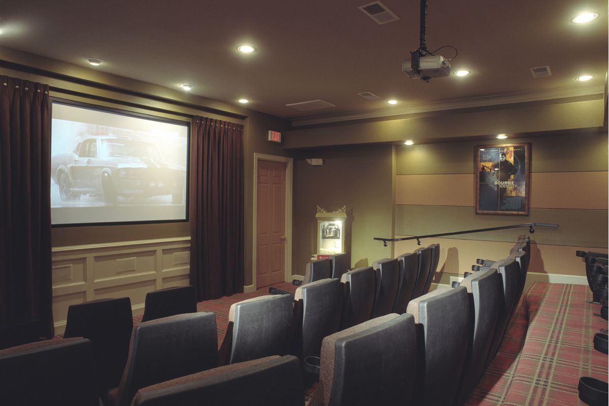 A small home theater with rows of seats, a projector, and a movie playing on a screen at the front.