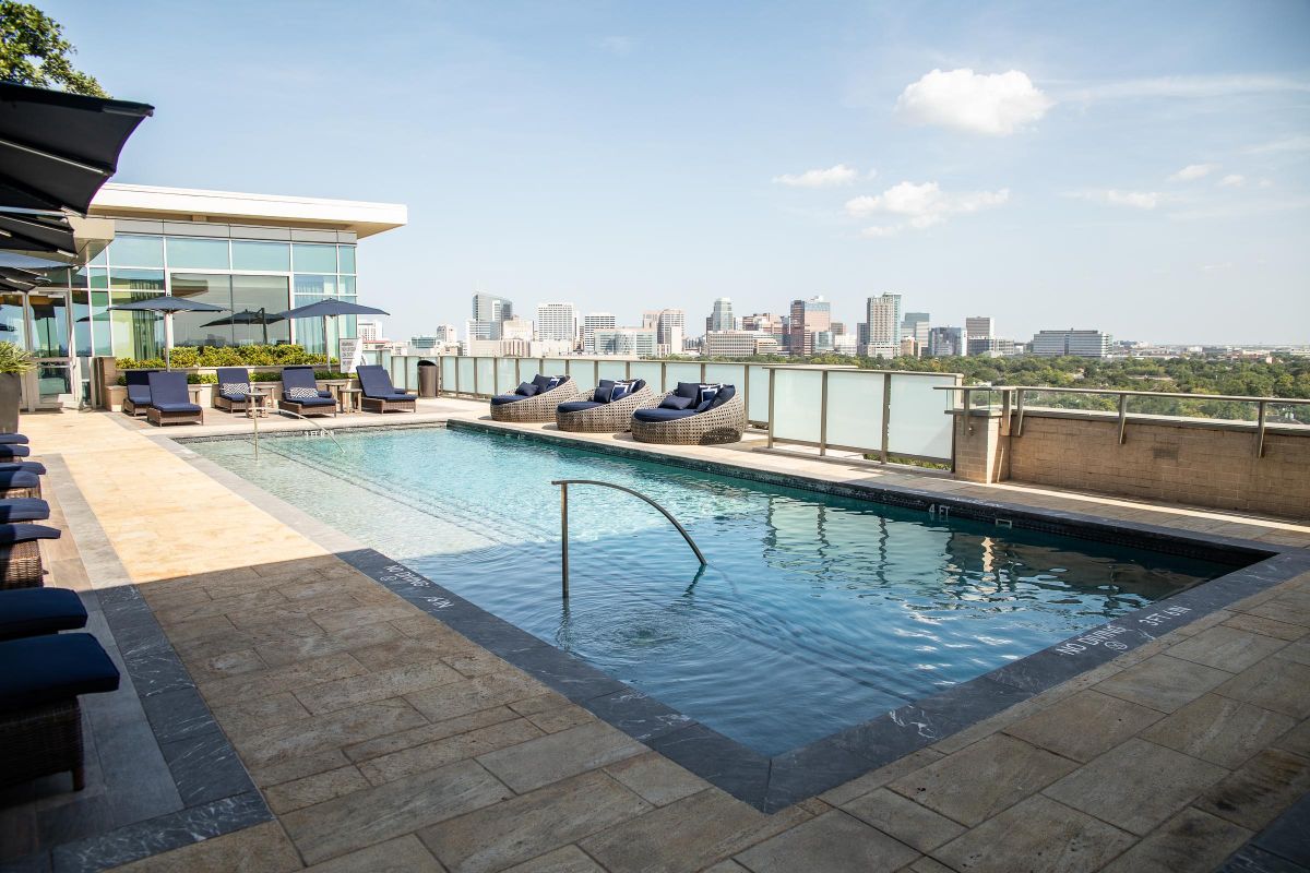 Rooftop pool with lounge chairs, city skyline in the background under a clear blue sky at Hanover Southampton apartments.