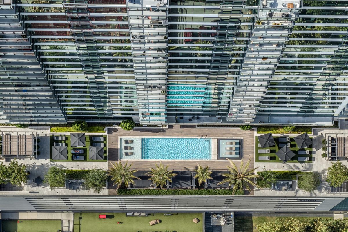 Aerial view of modern building with rooftop pool, lounge areas, and surrounding greenery.