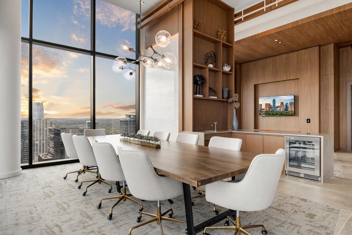 Modern dining room with a wooden table, white chairs, large windows and city view at sunset.