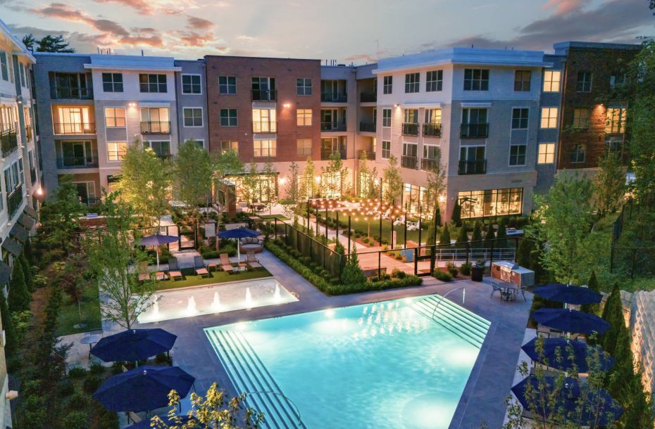 Hanover Company, Hanover Weymouth Modern apartment complex at dusk with a glowing pool and outdoor seating area, surrounded by trees and greenery.