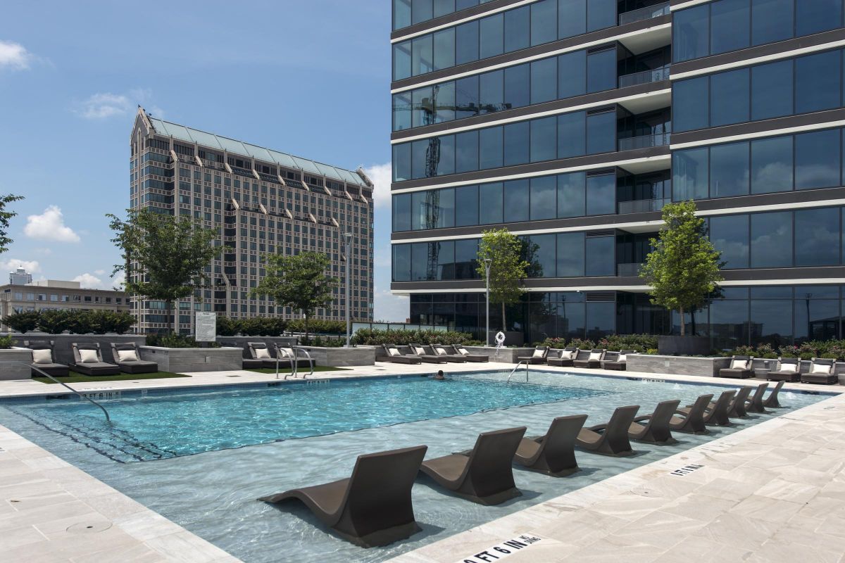 Outdoor pool with lounge chairs at a modern high-rise building, overlooking another tall building and clear skies.