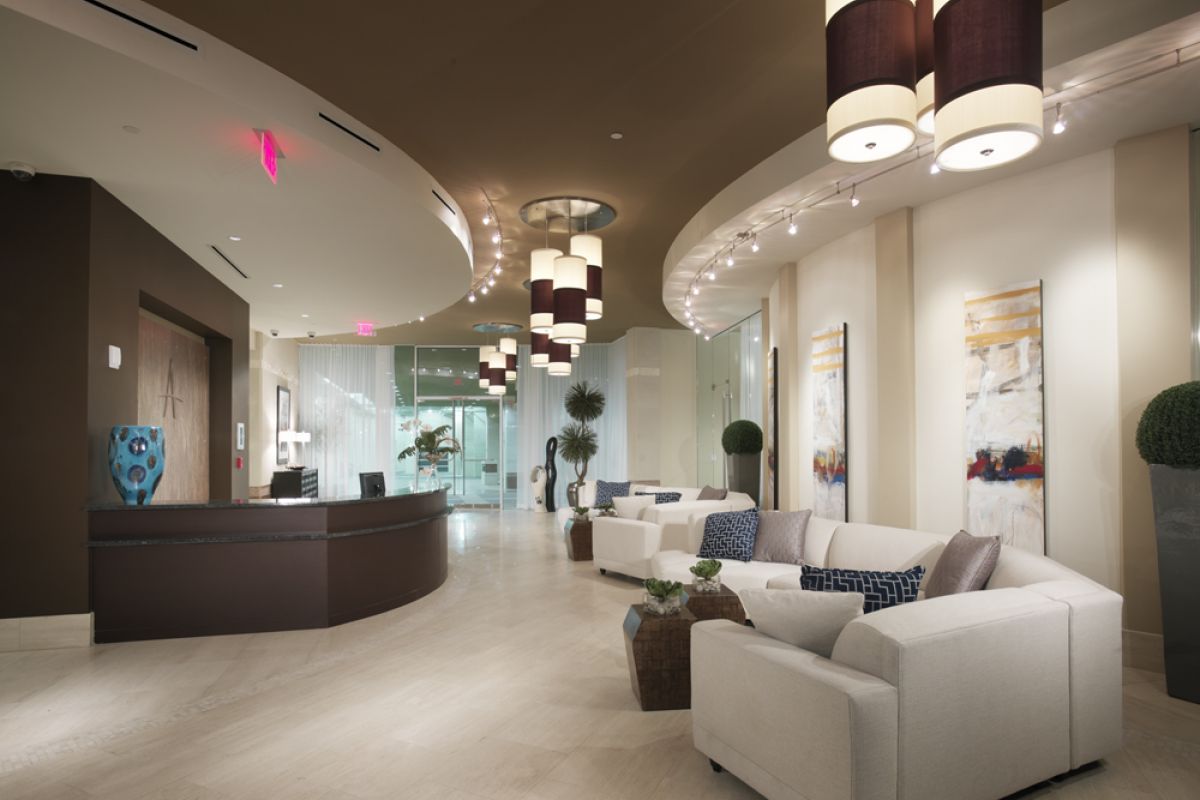 Modern Ashton Austin lobby with white sofas, abstract art, round reception desk, and pendant lights on a curved ceiling.