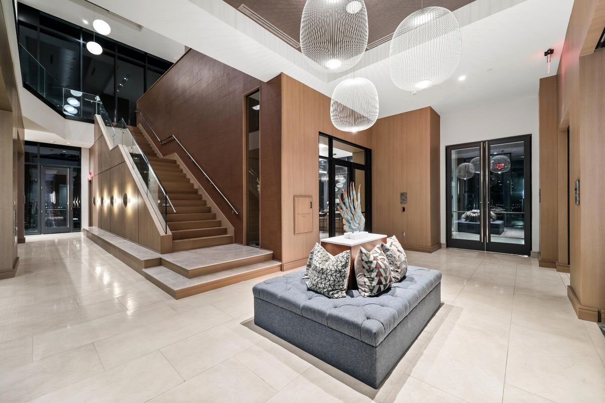 Modern lobby with stairs, large pendant lights, and a cushioned seating area with decorative pillows.