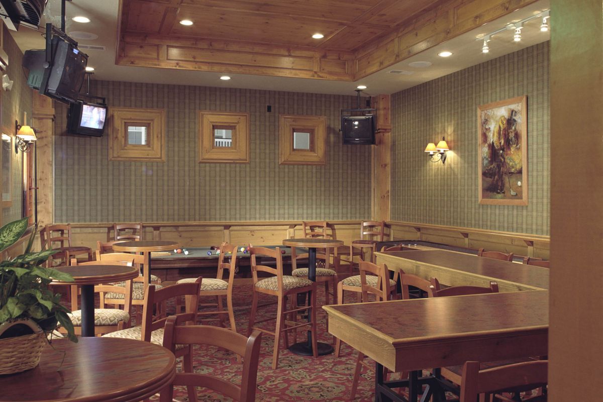A cozy, empty restaurant with wooden tables, chairs, wall decor, TVs, and patterned wallpaper.